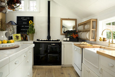 Inspiration for a scandinavian kitchen in Portland with a farmhouse sink, tile benchtops, open cabinets, white cabinets, black appliances and white splashback.