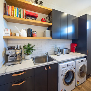 Design ideas for a medium sized contemporary single-wall separated utility room in Melbourne with a single-bowl sink, flat-panel cabinets, black cabinets, engineered stone countertops, white walls, light hardwood flooring, yellow floors and white worktops.