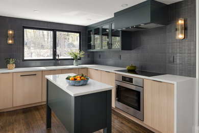 Contemporary l-shaped kitchen/diner in Boston with a submerged sink, flat-panel cabinets, light wood cabinets, engineered stone countertops, black splashback, porcelain splashback, stainless steel appliances, medium hardwood flooring, an island, brown floors and white worktops.