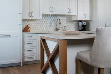 Mid-sized trendy single-wall medium tone wood floor and brown floor open concept kitchen photo in Other with an undermount sink, recessed-panel cabinets, white cabinets, white backsplash, ceramic backsplash, paneled appliances, an island and white countertops