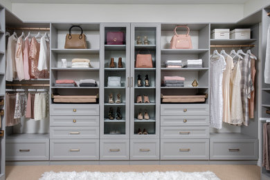 This is an example of a mid-sized modern women's walk-in wardrobe in Dallas with recessed-panel cabinets, grey cabinets, carpet and beige floor.