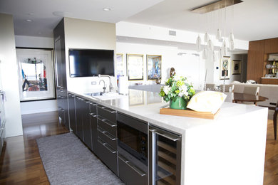 Photo of a mid-sized modern galley open plan kitchen in Los Angeles with a drop-in sink, flat-panel cabinets, stainless steel cabinets, solid surface benchtops, white splashback, stone slab splashback, stainless steel appliances, light hardwood floors and with island.