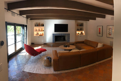 Modelo de cine en casa cerrado tradicional de tamaño medio con paredes blancas, suelo de baldosas de terracota, televisor colgado en la pared y suelo naranja