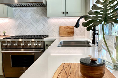 Example of a mid-sized arts and crafts u-shaped vinyl floor and brown floor kitchen design in San Diego with an undermount sink, shaker cabinets, green cabinets, white backsplash, ceramic backsplash, stainless steel appliances and an island