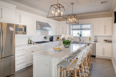 Inspiration for a mid-sized transitional l-shaped separate kitchen in New York with a farmhouse sink, shaker cabinets, white cabinets, quartzite benchtops, white splashback, subway tile splashback, stainless steel appliances, medium hardwood floors, with island, brown floor and white benchtop.