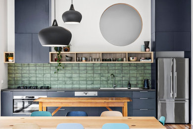 Design ideas for a mid-sized contemporary single-wall open plan kitchen in Melbourne with a drop-in sink, flat-panel cabinets, grey cabinets, solid surface benchtops, green splashback, ceramic splashback, stainless steel appliances, medium hardwood floors, with island and grey benchtop.
