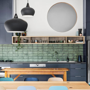 Design ideas for a mid-sized contemporary single-wall open plan kitchen in Melbourne with a drop-in sink, flat-panel cabinets, grey cabinets, solid surface benchtops, green splashback, ceramic splashback, stainless steel appliances, medium hardwood floors, with island and grey benchtop.
