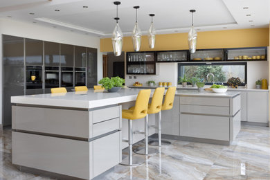 Photo of a large contemporary open plan kitchen in Hampshire with an integrated sink, glass-front cabinets, beige cabinets, engineered stone countertops, black appliances, porcelain flooring, an island, beige floors, beige worktops and feature lighting.