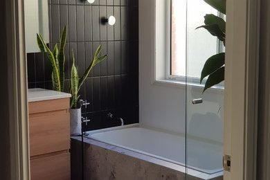 Mid-sized contemporary kids bathroom in Newcastle - Maitland with flat-panel cabinets, medium wood cabinets, a drop-in tub, a curbless shower, a two-piece toilet, multi-coloured tile, porcelain tile, multi-coloured walls, porcelain floors, an integrated sink, grey floor, a hinged shower door and white benchtops.