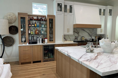 Example of a mid-sized beach style l-shaped light wood floor, brown floor and coffered ceiling kitchen pantry design in Other with an undermount sink, flat-panel cabinets, light wood cabinets, quartzite countertops, multicolored backsplash, stainless steel appliances, an island and multicolored countertops