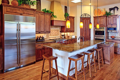 Mid-sized eclectic l-shaped kitchen in Albuquerque with raised-panel cabinets, dark wood cabinets, granite benchtops, beige splashback, ceramic splashback, stainless steel appliances, medium hardwood floors, with island and brown floor.