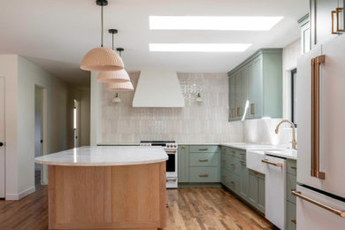 Mid-sized mid-century modern l-shaped light wood floor eat-in kitchen photo in Boise with a farmhouse sink, shaker cabinets, green cabinets, quartz countertops, white backsplash, ceramic backsplash, white appliances, an island and white countertops