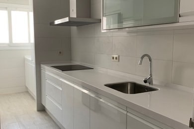 Modelo de cocina lineal minimalista pequeña cerrada sin isla con fregadero bajoencimera, armarios con paneles lisos, puertas de armario blancas, encimera de cuarzo compacto, salpicadero blanco, salpicadero de azulejos de cerámica, electrodomésticos de acero inoxidable, suelo de baldosas de cerámica, suelo gris y encimeras blancas