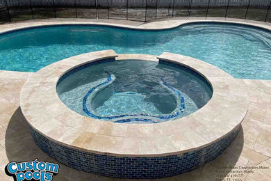 Mid-sized tropical backyard custom-shaped natural pool in Miami with a hot tub and natural stone pavers.