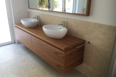 Geräumiges Modernes Badezimmer En Suite mit flächenbündigen Schrankfronten, braunen Schränken, bodengleicher Dusche, Toilette mit Aufsatzspülkasten, beigen Fliesen, Steinplatten, beiger Wandfarbe, Kalkstein, Aufsatzwaschbecken, Waschtisch aus Holz, beigem Boden und offener Dusche in Hamburg