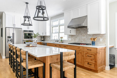 This is an example of a large country l-shaped eat-in kitchen in Boston with an undermount sink, recessed-panel cabinets, white cabinets, quartz benchtops, beige splashback, ceramic splashback, stainless steel appliances, light hardwood floors, with island, brown floor and white benchtop.
