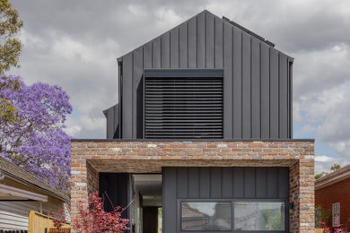 Photo of a mid-sized contemporary two-storey black house exterior in Sydney with metal siding and a gable roof.