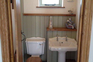 Photo of a small traditional shower room bathroom in Cambridgeshire with glass-front cabinets, medium wood cabinets, a built-in shower, a one-piece toilet, stone tiles, green walls, dark hardwood flooring, a pedestal sink, wooden worktops, a hinged door, brown worktops, a shower bench, a built in vanity unit, exposed beams and panelled walls.