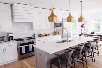 Mid-sized minimalist single-wall light wood floor and brown floor eat-in kitchen photo in Atlanta with a double-bowl sink, shaker cabinets, white cabinets, white backsplash, stainless steel appliances, an island and white countertops