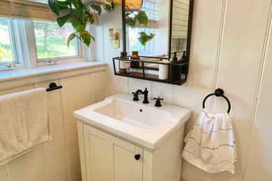 Example of a small farmhouse 3/4 white tile and ceramic tile laminate floor, brown floor, single-sink and wall paneling corner shower design in New York with shaker cabinets, white cabinets, a two-piece toilet, white walls, a drop-in sink, solid surface countertops, a hinged shower door, a niche and a freestanding vanity