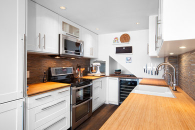 Photo of a mid-sized modern u-shaped eat-in kitchen in Vancouver with a farmhouse sink, beaded inset cabinets, white cabinets, wood benchtops, multi-coloured splashback, matchstick tile splashback, stainless steel appliances and a peninsula.