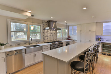 Inspiration for a large transitional u-shaped light wood floor and beige floor eat-in kitchen remodel in Philadelphia with a farmhouse sink, recessed-panel cabinets, white cabinets, quartz countertops, gray backsplash, matchstick tile backsplash, stainless steel appliances, an island and white countertops