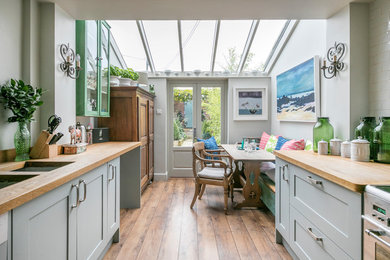 This is an example of a country galley eat-in kitchen in Hampshire with an undermount sink, shaker cabinets, grey cabinets, wood benchtops, white splashback, subway tile splashback, stainless steel appliances, dark hardwood floors, no island, brown floor and brown benchtop.