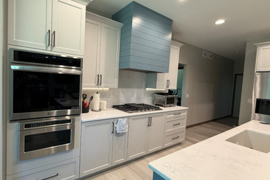 Example of a mid-sized trendy l-shaped light wood floor and white floor open concept kitchen design in Other with an undermount sink, shaker cabinets, white cabinets, quartzite countertops, white backsplash, quartz backsplash, stainless steel appliances, an island and white countertops