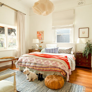 Réalisation d'une chambre bohème avec un mur blanc, un sol en bois brun et un sol orange.