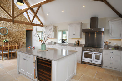 Photo of a traditional kitchen/diner in Gloucestershire with a double-bowl sink, recessed-panel cabinets, quartz worktops, metal splashback, stainless steel appliances, limestone flooring and an island.