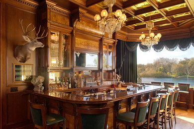 Example of a huge classic u-shaped medium tone wood floor seated home bar design in Other with glass-front cabinets, medium tone wood cabinets, wood countertops, multicolored backsplash, mirror backsplash and brown countertops