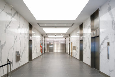 Large trendy ceramic tile, gray floor and tray ceiling hallway photo in New York with white walls