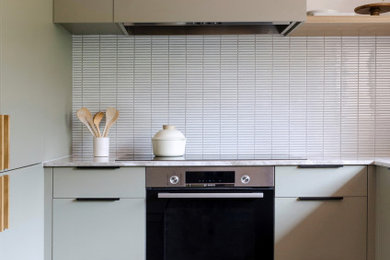This is an example of a mid-sized midcentury u-shaped kitchen pantry in Melbourne with a single-bowl sink, flat-panel cabinets, green cabinets, limestone benchtops, white splashback, mosaic tile splashback, black appliances, slate floors, a peninsula, brown floor and beige benchtop.