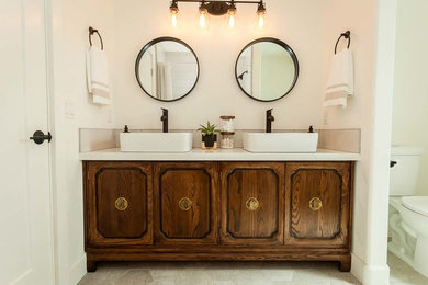 Inspiration for a mid-sized country bathroom in San Luis Obispo with recessed-panel cabinets, dark wood cabinets, a two-piece toilet, white walls, ceramic floors, a vessel sink, engineered quartz benchtops, grey floor and white benchtops.