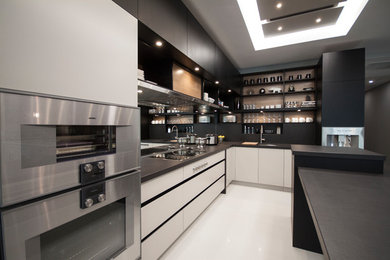 Cette image montre une cuisine design en L de taille moyenne avec un placard à porte plane, des portes de placard blanches, un électroménager en acier inoxydable et îlot.