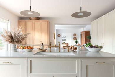This is an example of a large scandi grey and cream kitchen/diner in Surrey with an integrated sink, shaker cabinets, light wood cabinets, quartz worktops, grey splashback, black appliances, light hardwood flooring, an island and grey worktops.