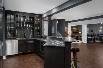Photo of a large traditional u-shaped seated home bar in Chicago with dark hardwood floors, brown floor, an undermount sink, glass-front cabinets, black cabinets, marble benchtops, black splashback, stone slab splashback and black benchtop.