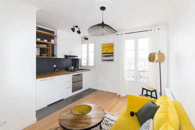 Idée de décoration pour une petite cuisine américaine linéaire et noire et bois minimaliste avec un évier encastré, un placard à porte plane, des portes de placard blanches, un plan de travail en bois, une crédence noire, un électroménager en acier inoxydable, un sol en carrelage de céramique, un sol noir et fenêtre au-dessus de l'évier.
