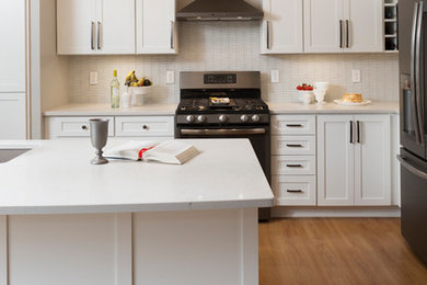 Example of a mid-sized transitional l-shaped vinyl floor and beige floor kitchen design in Milwaukee with an undermount sink, shaker cabinets, white cabinets, quartzite countertops, white backsplash, glass tile backsplash, stainless steel appliances and an island