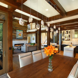 Cette image montre une grande salle à manger ouverte sur le salon craftsman avec un mur blanc, un sol en bois clair, une cheminée standard et un manteau de cheminée en pierre.