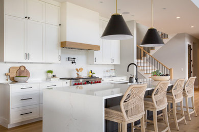 Large farmhouse l-shaped light wood floor and brown floor open concept kitchen photo in Seattle with an undermount sink, shaker cabinets, white cabinets, quartz countertops, white backsplash, quartz backsplash, stainless steel appliances, an island and white countertops