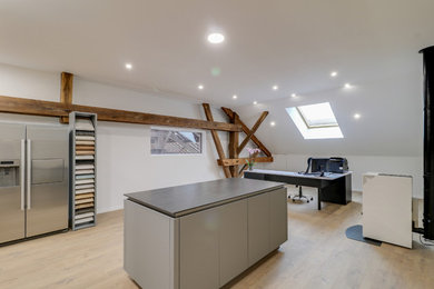 Cette photo montre un grand bureau moderne avec un mur blanc, parquet clair, un poêle à bois, un manteau de cheminée en métal et un bureau indépendant.