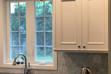 Mid-sized trendy l-shaped dark wood floor eat-in kitchen photo in New York with an undermount sink, recessed-panel cabinets, white cabinets, granite countertops, gray backsplash, stone tile backsplash, stainless steel appliances and an island
