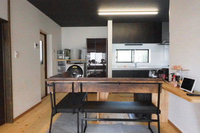Foto de cocina lineal y gris y negra moderna grande abierta con puertas de armario negras, encimera de acrílico, salpicadero blanco, suelo de madera clara, encimeras grises y papel pintado