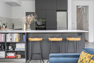 This is an example of a medium sized modern grey and white u-shaped open plan kitchen in London with a built-in sink, flat-panel cabinets, black cabinets, marble worktops, yellow splashback, marble splashback, black appliances, ceramic flooring, a breakfast bar, grey floors and white worktops.