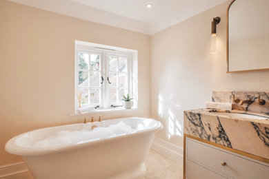 Inspiration for a large classic ensuite bathroom in Surrey with shaker cabinets, white cabinets, a freestanding bath, a wall mounted toilet, beige tiles, marble tiles, beige walls, marble flooring, a built-in sink, marble worktops, beige floors, a hinged door, pink worktops, a wall niche, double sinks and a freestanding vanity unit.