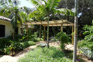 This is an example of a mid-sized tropical backyard full sun garden for summer in Miami with natural stone pavers.