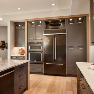 Aménagement d'une grande arrière-cuisine contemporaine avec un placard à porte plane, des portes de placard grises, un plan de travail en quartz, une crédence grise, une crédence en carrelage de pierre, un électroménager de couleur, un sol en bois clair et un îlot central.