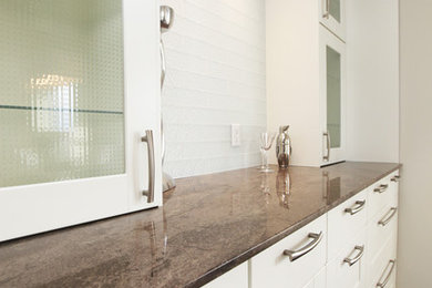 Trendy single-wall dark wood floor wet bar photo in Calgary with glass-front cabinets, white cabinets, granite countertops, white backsplash, glass tile backsplash and no sink