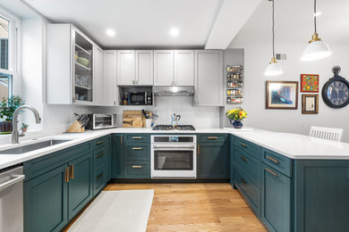 Example of a mid-sized transitional u-shaped light wood floor and brown floor enclosed kitchen design in Philadelphia with an undermount sink, shaker cabinets, green cabinets, quartzite countertops, white backsplash, ceramic backsplash, white appliances, a peninsula and white countertops